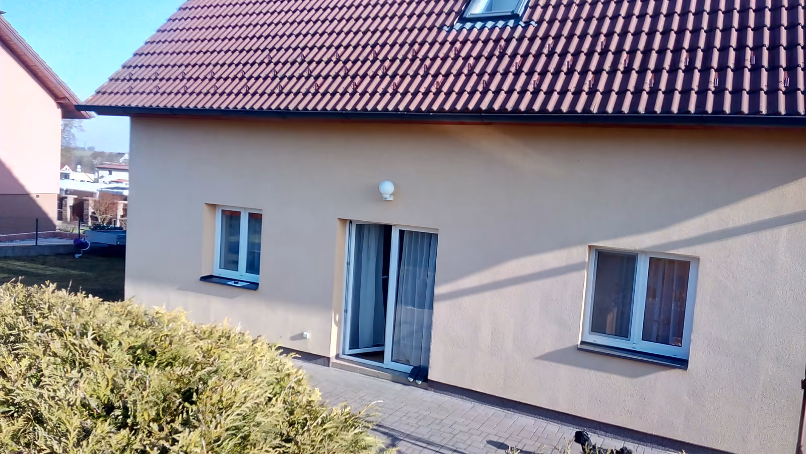 otevřená dlážděná terasa u béžového domu s bílými dveřmi