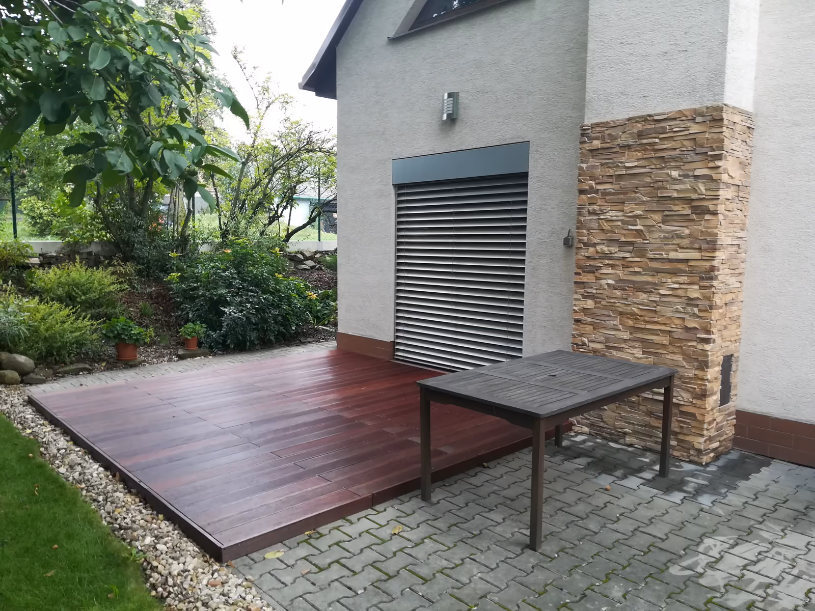 otevřená dřevěná terasa a zámková dlažba u kamenného sloupu