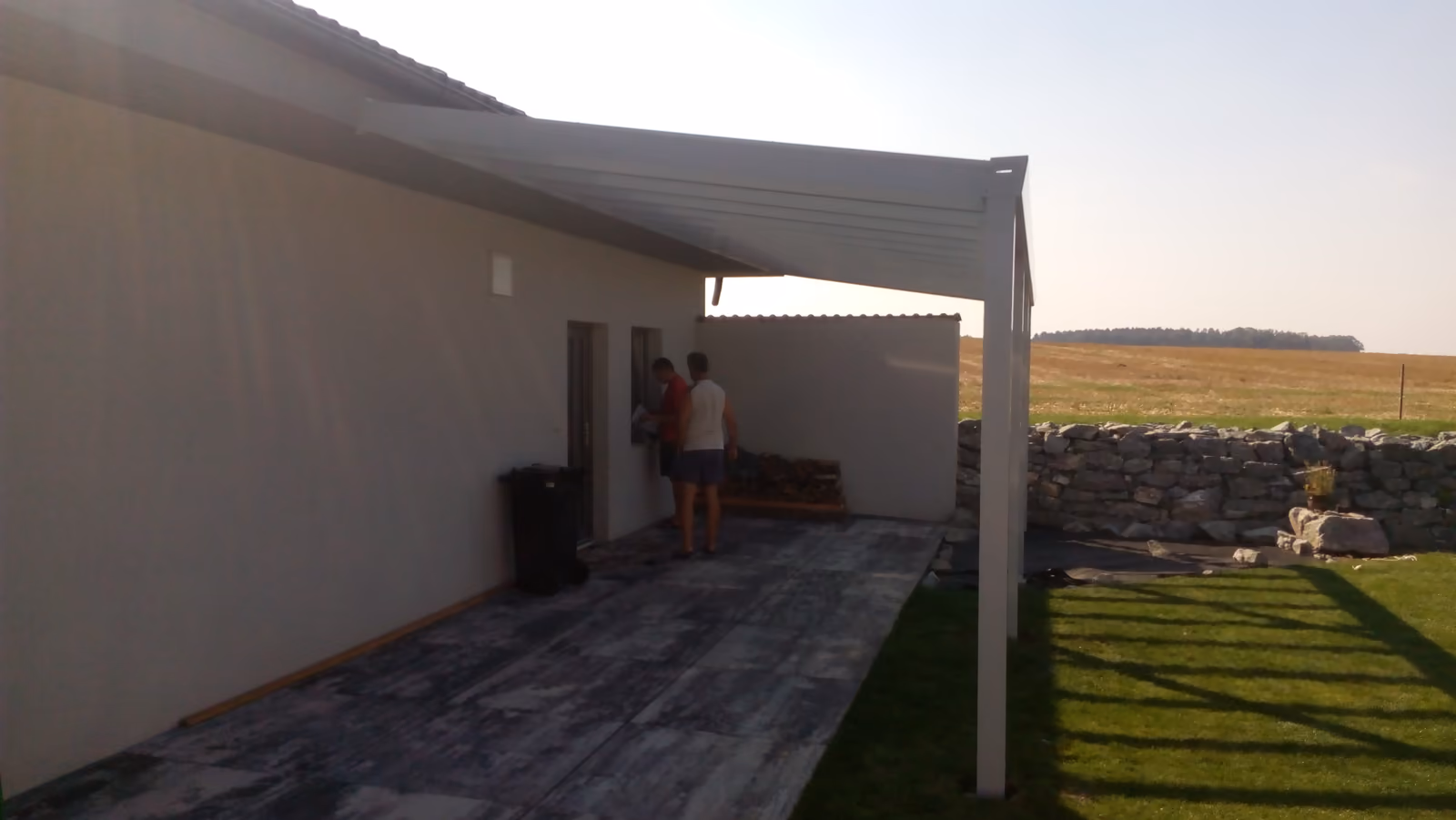 bílá hliníková pergola nad šedou dlažbou u světlého domu