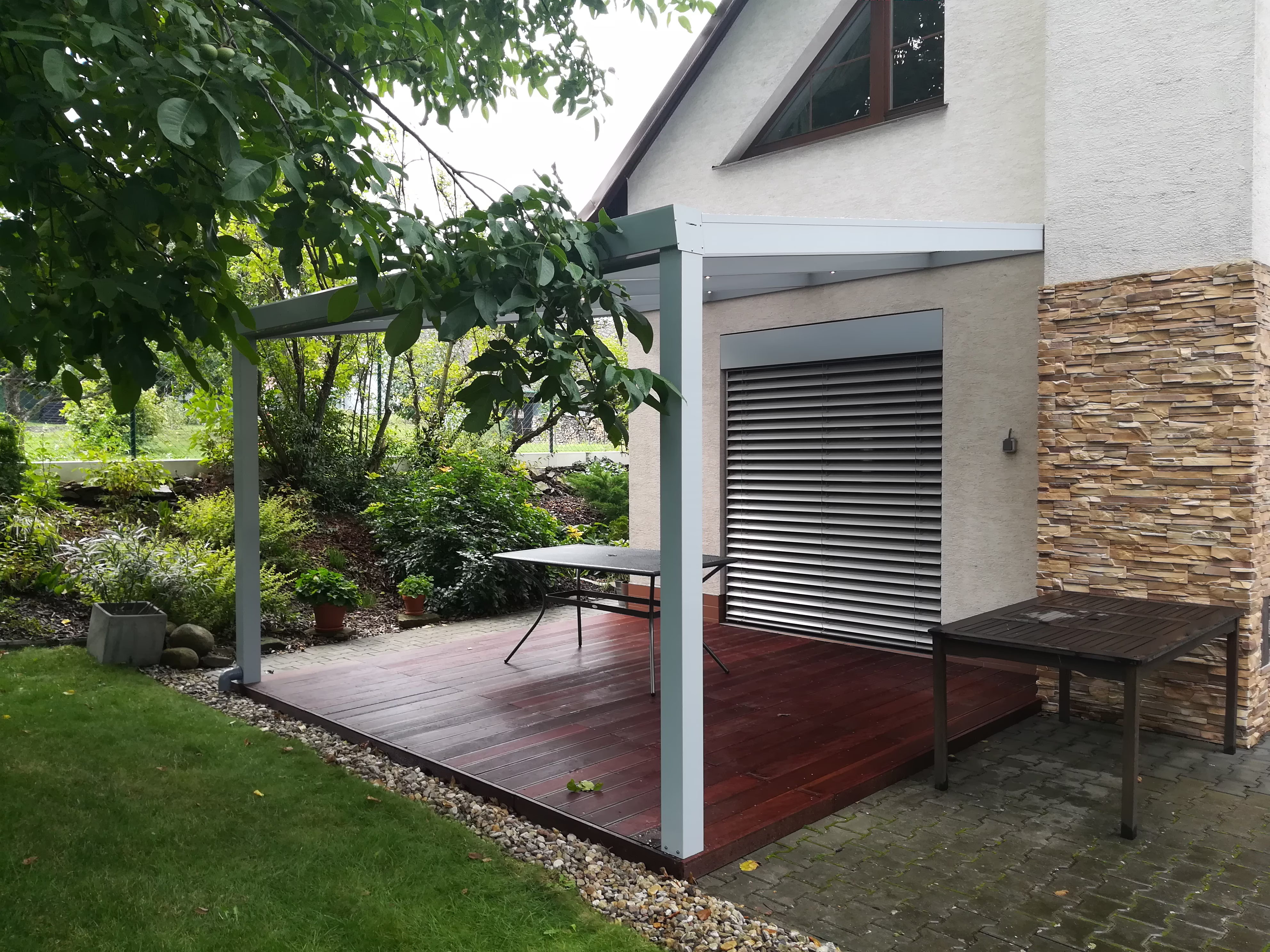 stříbrná hliníková pergola nad tmavou dřevěnou terasou