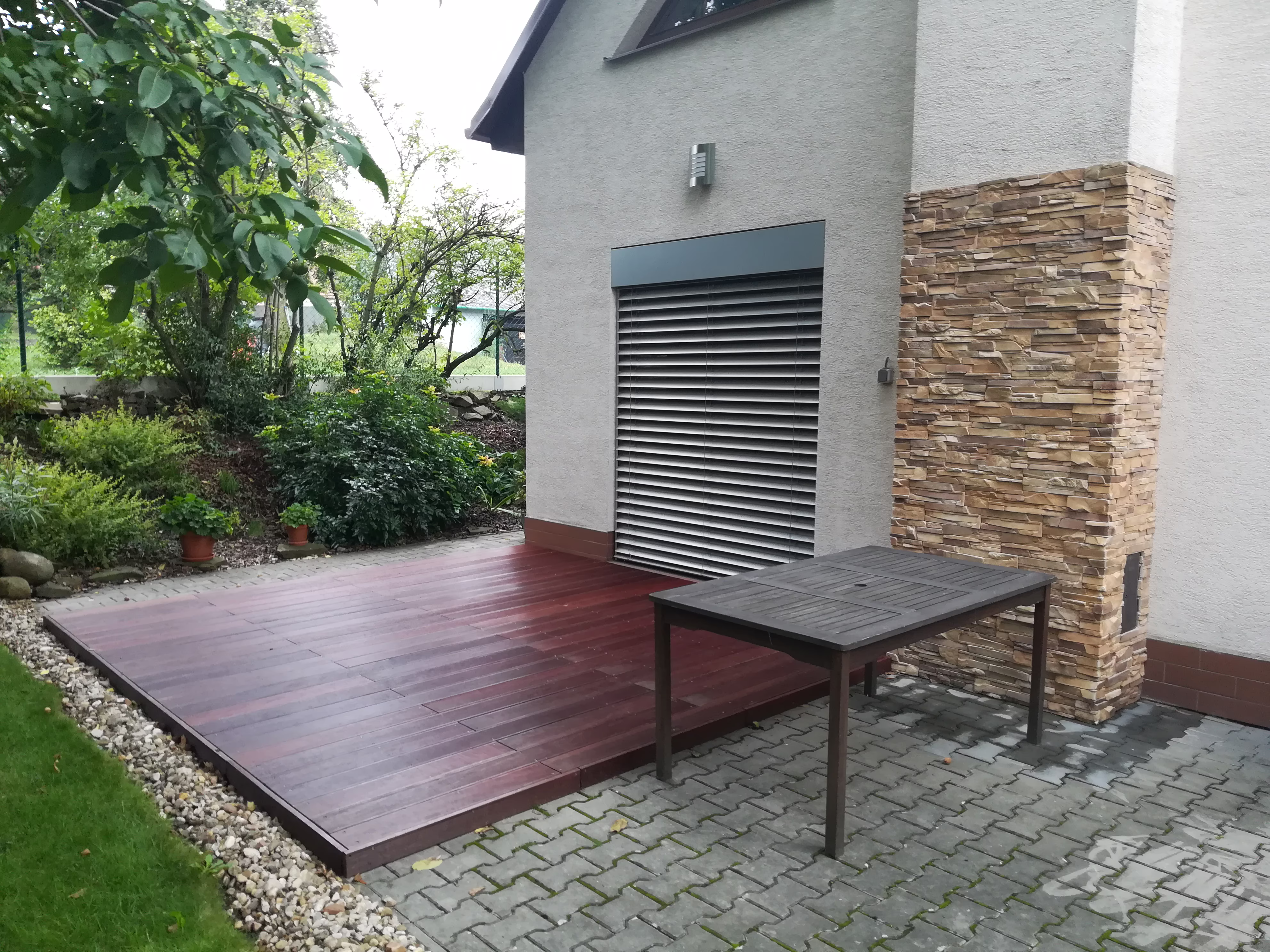 otevřená dřevěná terasa a zámková dlažba u kamenného sloupu