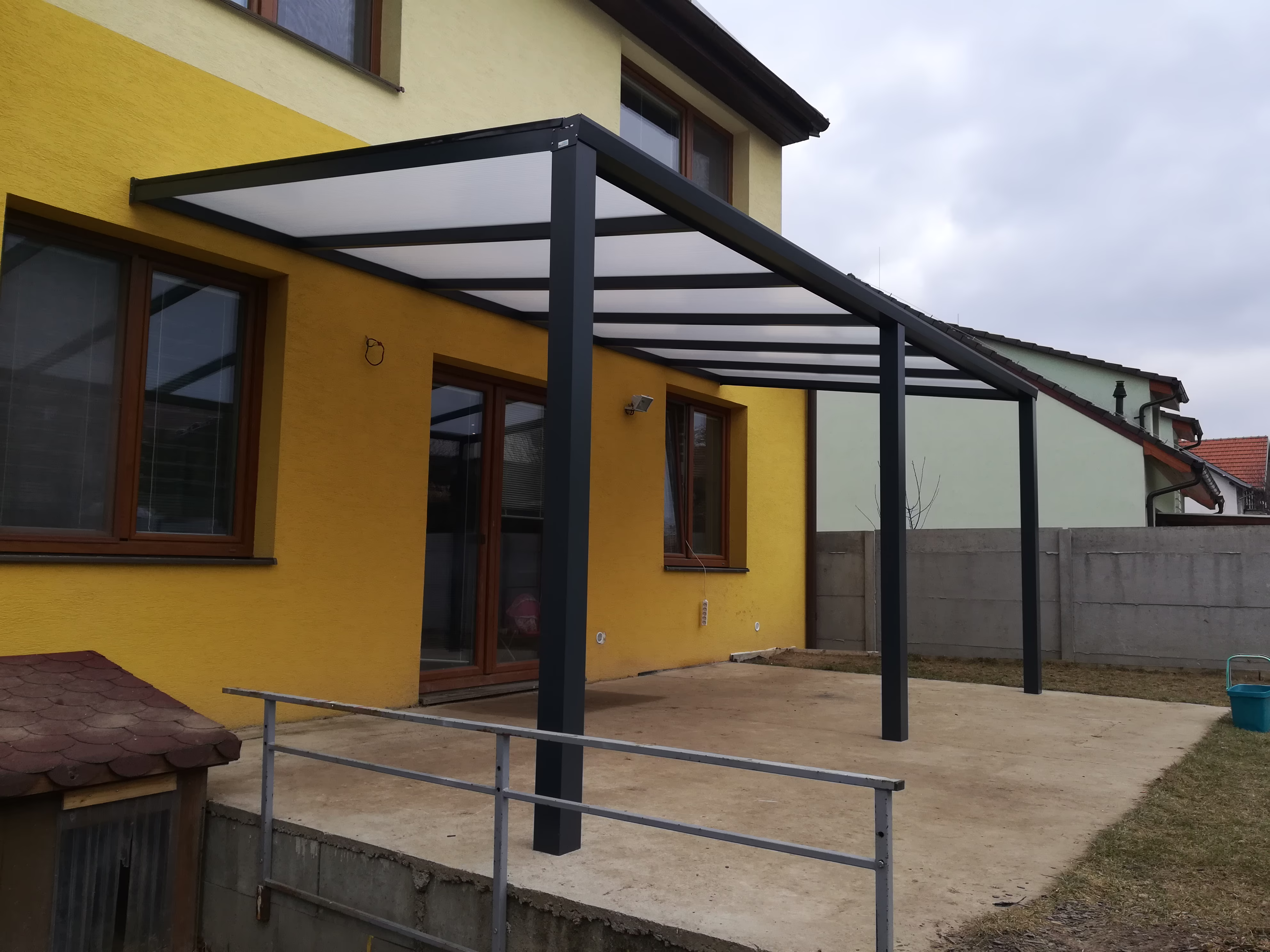 antracitová pergola ECO s opálovou střechou u žlutého domu