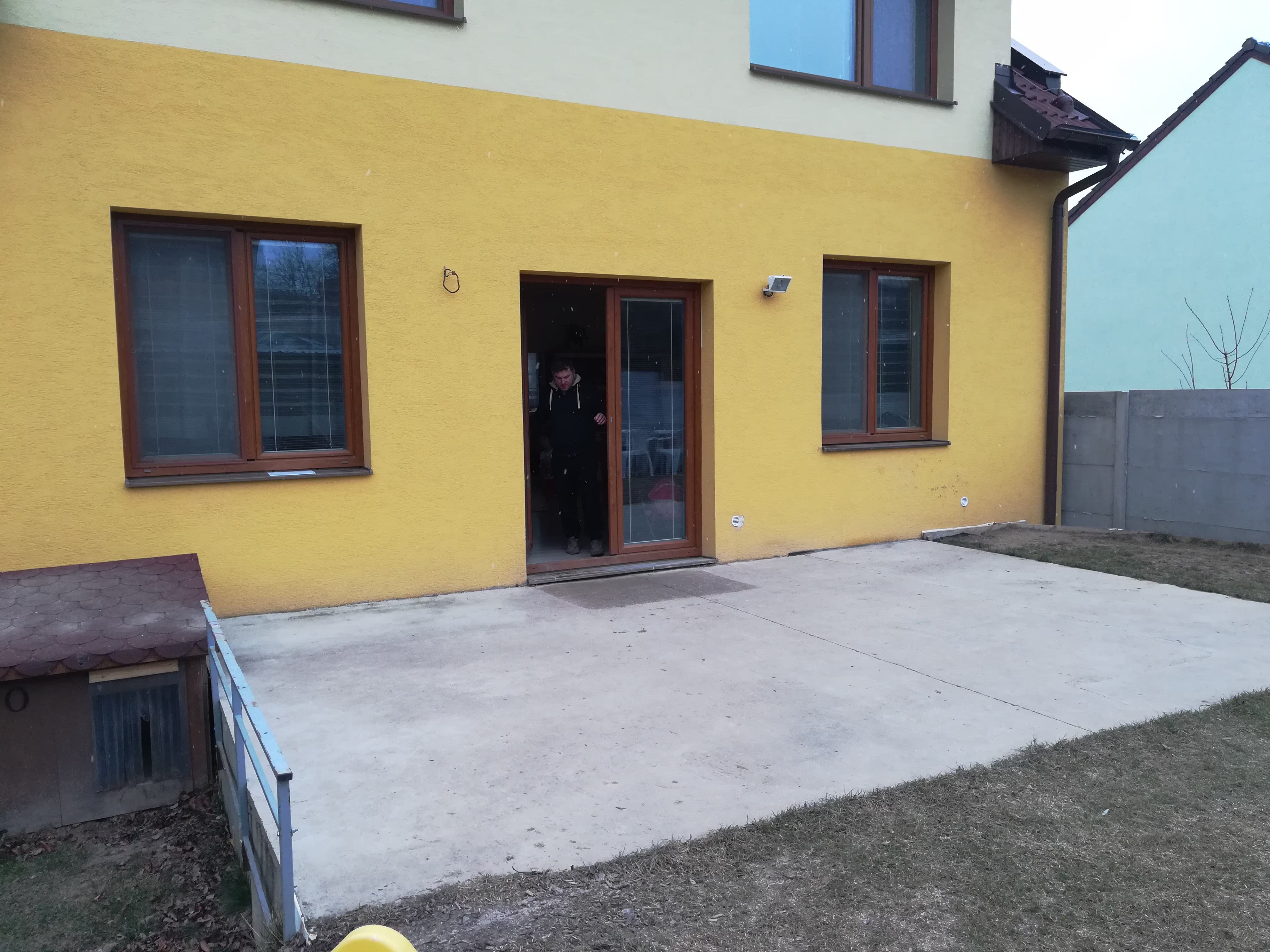 holá betonová deska u žlutého domu s hnědými dveřmi