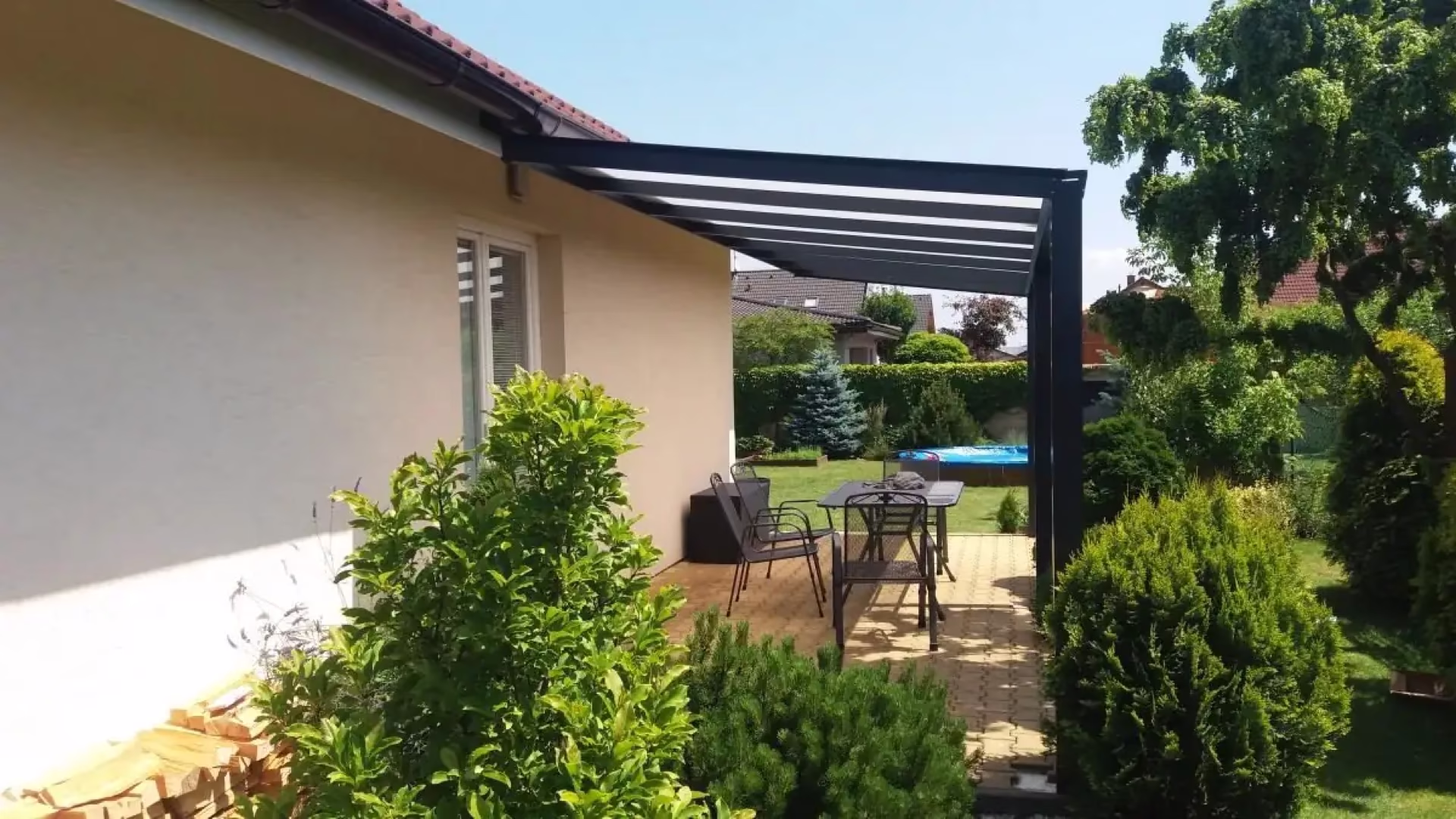 černá hliníková pergola u krémového domu se zahradním stolem