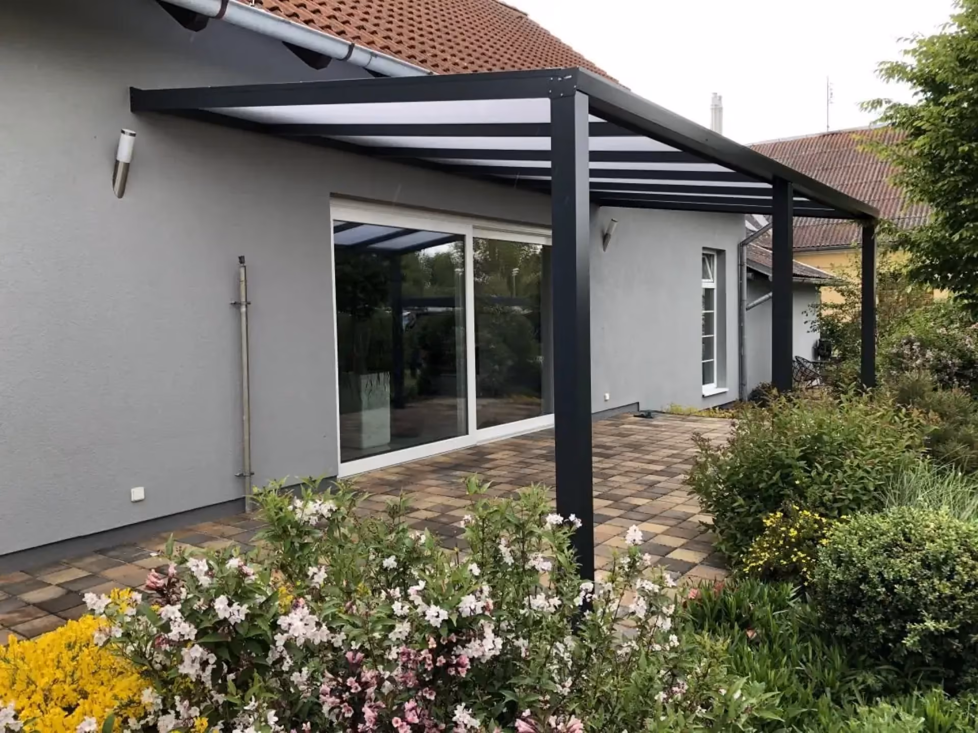 antracitová pergola u šedého domu nad kamennou terasou