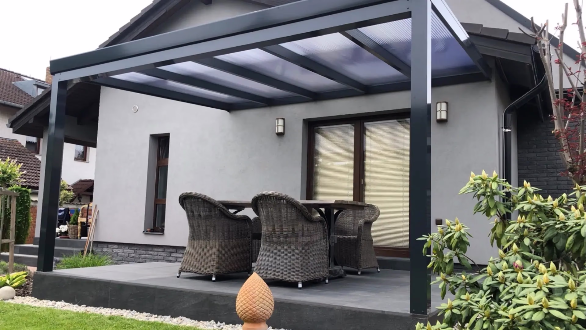 Hliníková pergola nad terasou s ratanovým sezením a místem na vaření